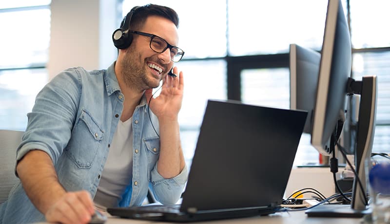 man with headset sitting in front of a laptop smiling